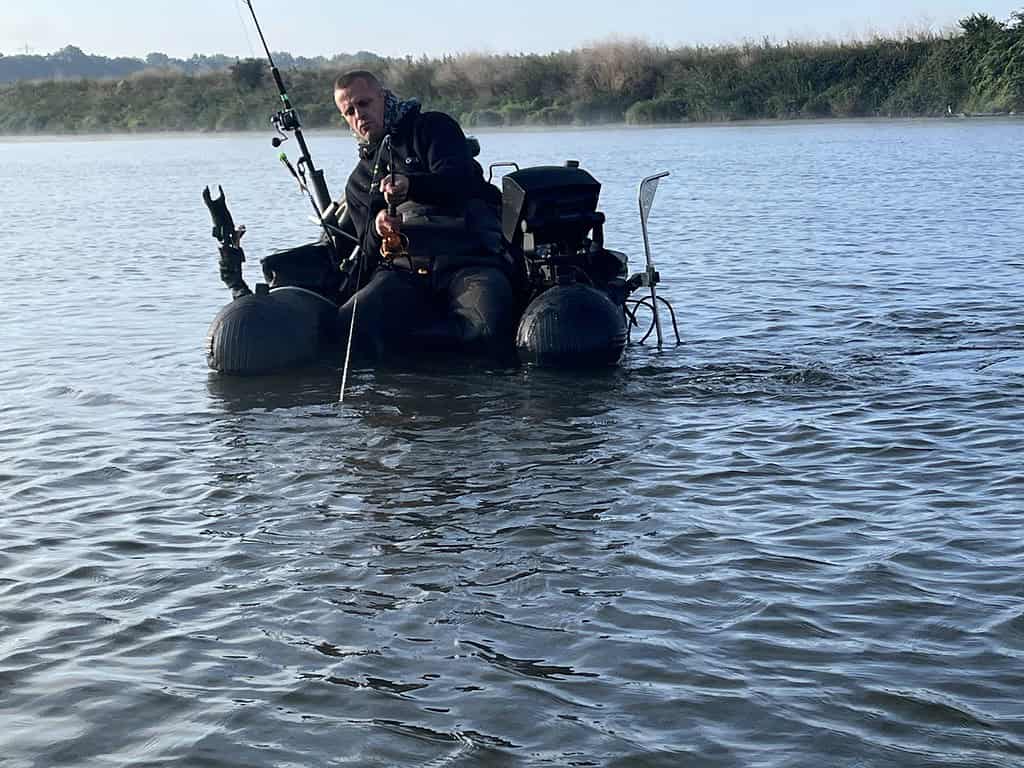 Paul Breems is in een waterscooter aan het vissen in een water met riet en bomen op de achtergrond, in de hoop een XXL-meerval te vangen.