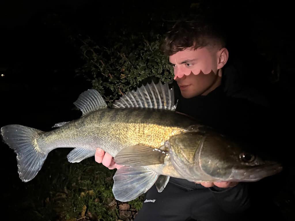 Een persoon houdt's nachts trots een grote vis vast, met struiken op de achtergrond. Dit is een van de'dikke bakken' uit de'vangsten van de week' van deze week.