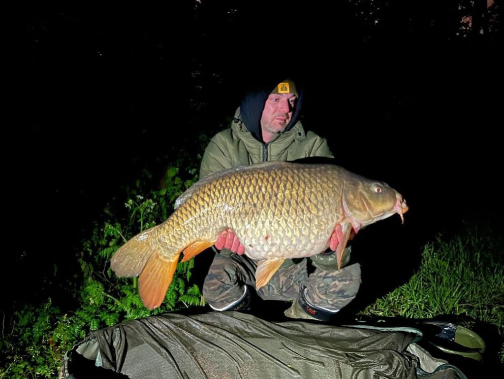 Een persoon houdt's nachts trots een grote karper vast, gekleed in een warme jas en muts, omringd door zijn visgerei. Deze indrukwekkende vangsten draagt bij aan hun prestaties van de week, en toont een gemengd palet aan hengelvaardigheden.