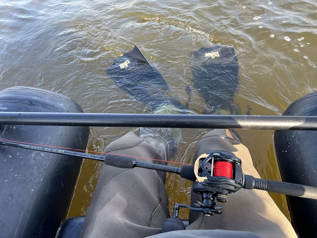 Een persoon in een opblaasbare buis is rustig aan het vissen, waarbij de vinnen door het water glijden. Hij houdt behendig een hengel vast met daaraan een rode haspel. Het doet denken aan de avonturen uit hoofdstuk acht.