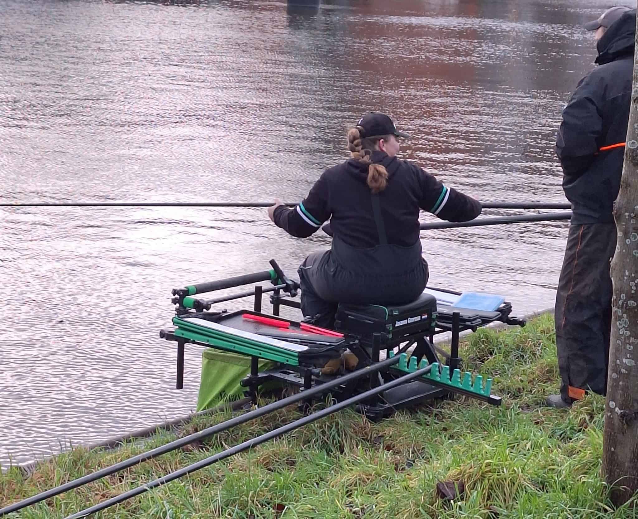 Gekleed in visgerei zit de persoon op de oever met een arsenaal aan apparatuur, alsof hij wordt aangestuurd door automatische concepten, terwijl hij een hengel boven het water houdt.