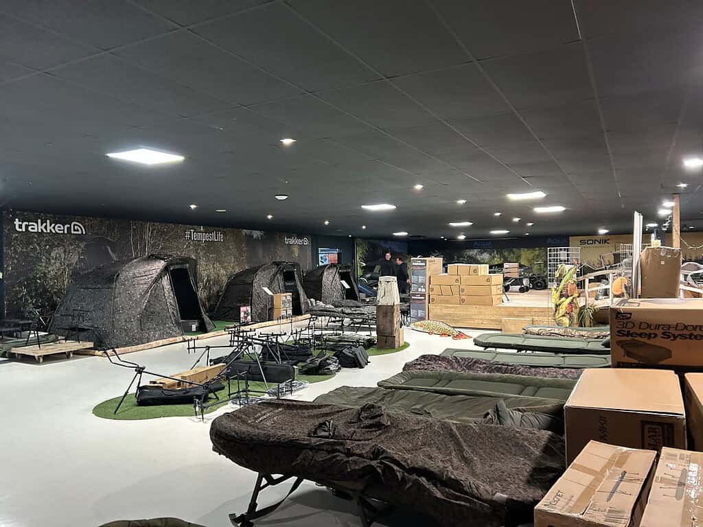 Ontdek de Hareco indoor camping gear store, met tenten van topkwaliteit, slaapsystemen en andere essentiële kampeerbenodigdheden. Alles is kunstig tentoongesteld op een witte vloer met een strak zwart plafond, wat de perfecte setting creëert voor uw volgende avontuur.