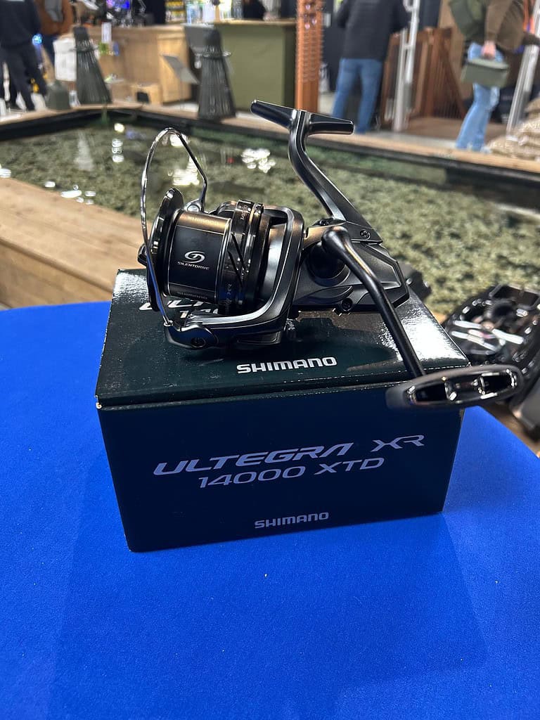 De Shimano-vismolen schittert op een blauw oppervlak, elegant gemonteerd op een Ultegra XR 14000 XTD-box, met een serene vijver als perfecte achtergrond.