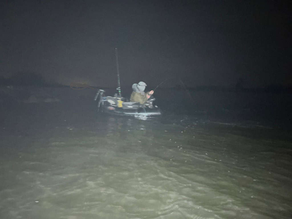 Persoon in een boot op donker water, 's nachts aan het vissen.