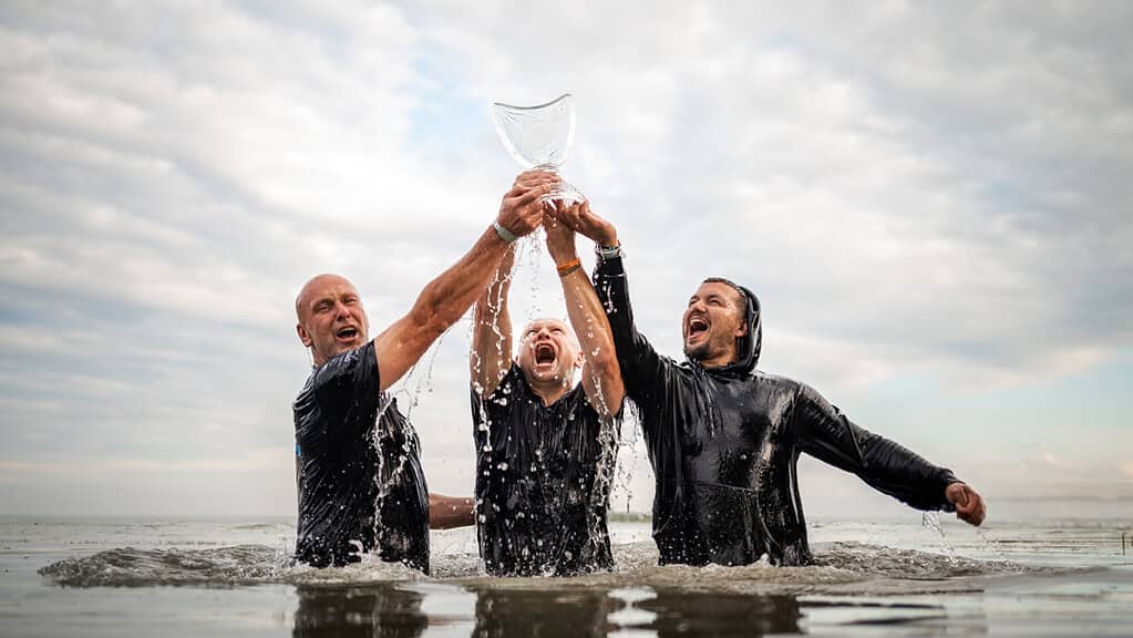 Drie mannen staan in het water van Lac de Madine, houden samen een trofee omhoog en juichen met een brede glimlach na hun overwinning in de De World Carp Classic 2024.