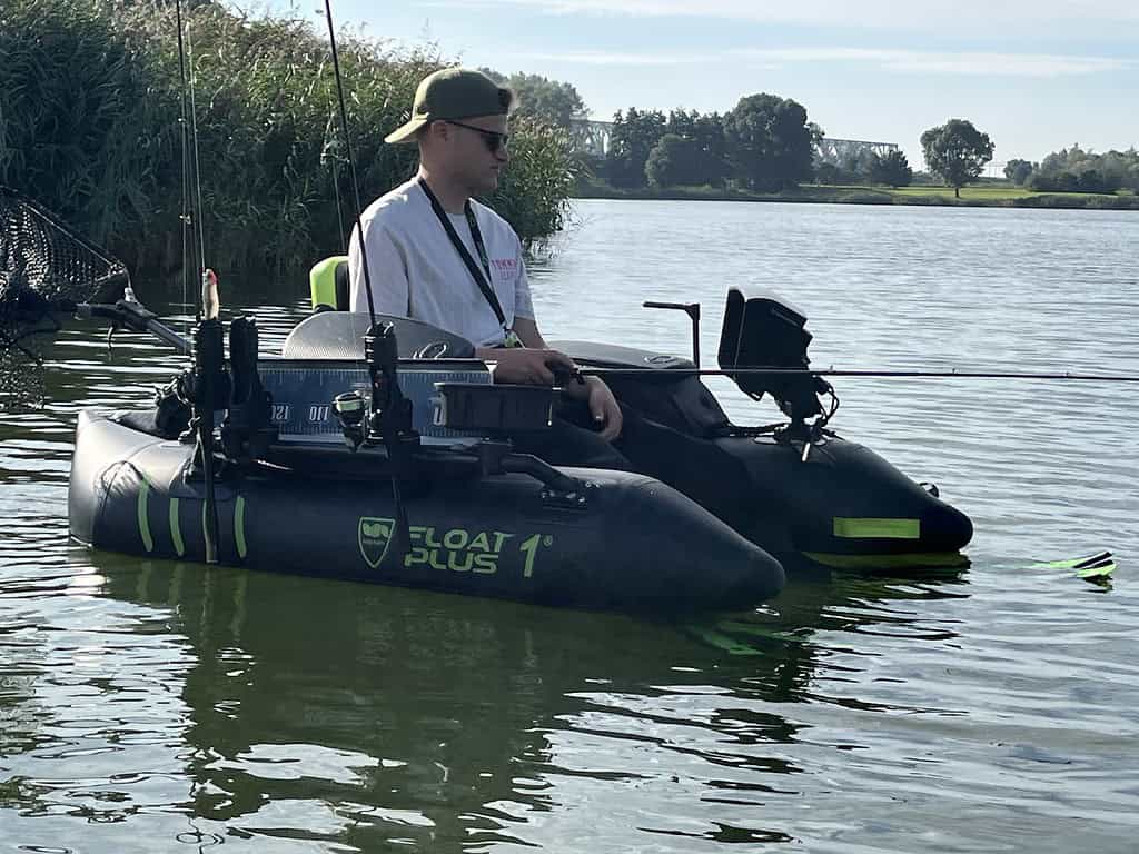 Een man zit op een opblaasbare bellyboat met visgerei, drijvend op een kalm meer nabij het riet op een heldere dag, genietend van een rustig dagje sportvissen.