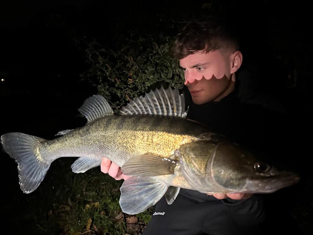 Een persoon houdt 's nachts trots een grote vis vast, met struiken op de achtergrond. Dit is een van de 'dikke bakken' uit de 'vangsten van de week' van deze week.