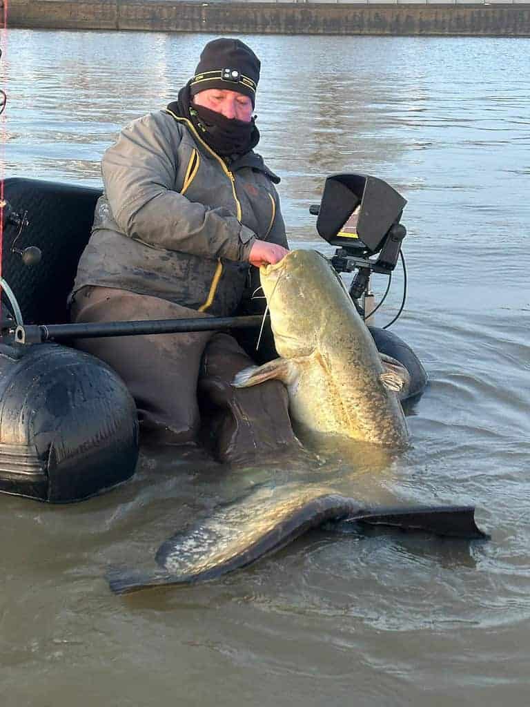 Een persoon op een drijvende stoel houdt een grote vangsten vast in het water, uitgerust met visgerei. Dit is de perfecte manier om de Blue Monday-blues te ontvluchten.