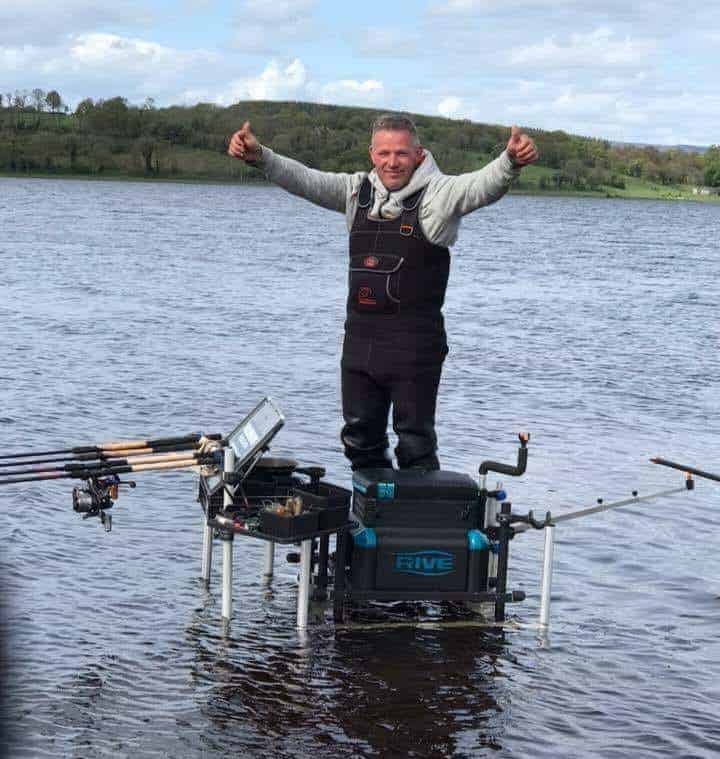 Trots staande op een visplatform in het serene water steekt Jan-Willem Plekkenpol zijn duim omhoog. Hengels en lokvoeders, speciaal aas, liggen verspreid en beloven een succesvolle vangst.