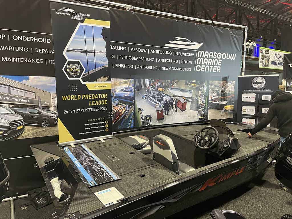 Een vissersboot wordt tentoongesteld in een maritiem centrum, wat doet denken aan de levendige displays die je zou vinden op Angelmesse Duisburg. Promotionele banners en afbeeldingen van maritieme diensten sieren de achtergrond, wat de nautische ambiance versterkt.