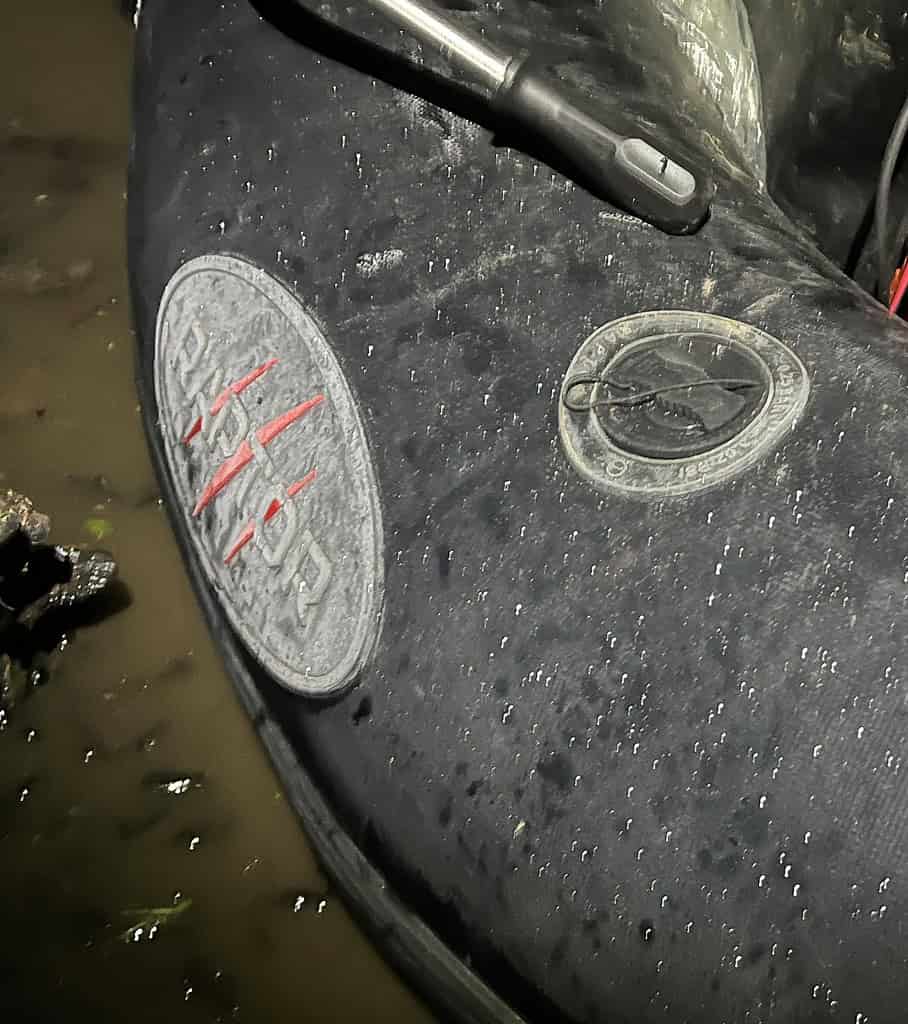 Close-up van een natte opblaasboot met een peddelhandvat erop, dat lijkt op een veerkrachtig monster dat klaar is voor de strijd. Het oppervlak van de boot heeft zichtbare ronde en ovale plekken.