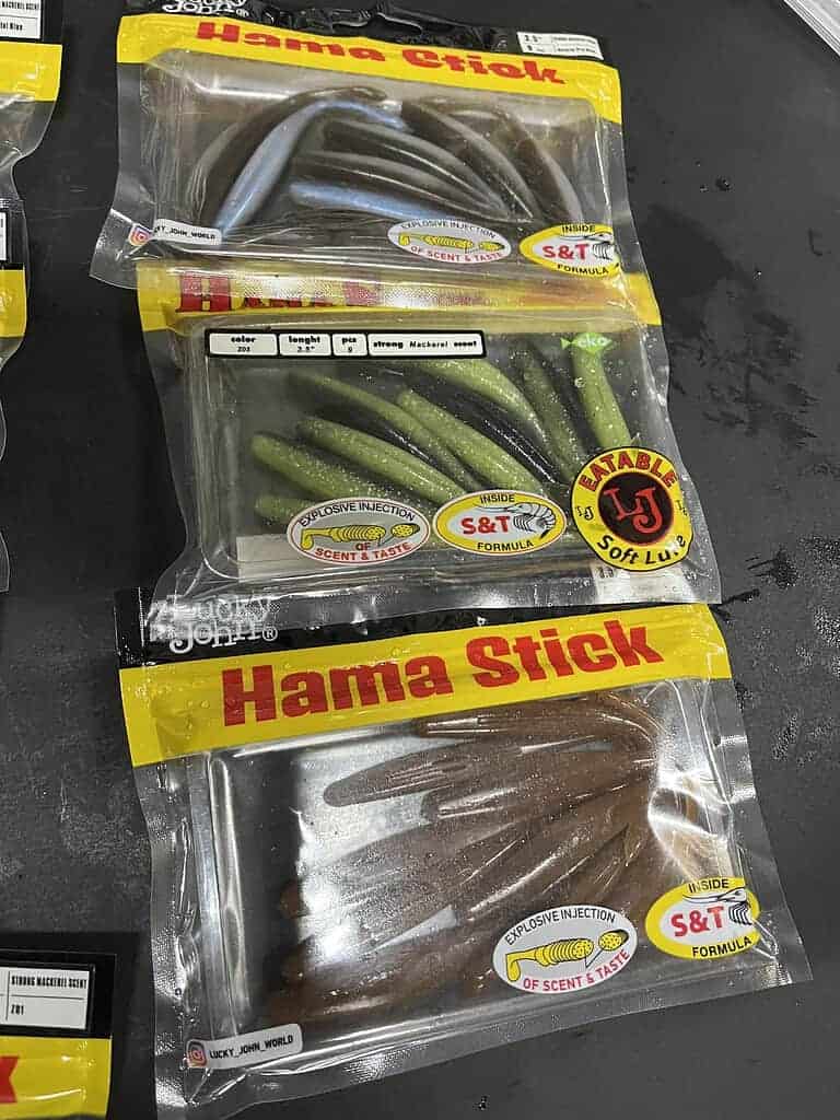 Plastic vislokmiddelen in verzegelde verpakkingen met het opschrift "Hama Stick", in verschillende kleurvariaties, tentoongesteld op een donkere ondergrond, wat doet denken aan de kwaliteitsuitrusting die te vinden is bij Hengelsport Zaltbommel in de Bommelerwaard.