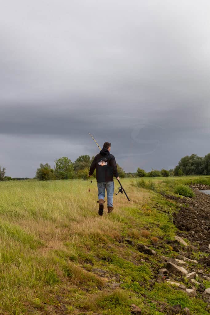 Een visser met vastloodsysteem wandelt langs een rivier
